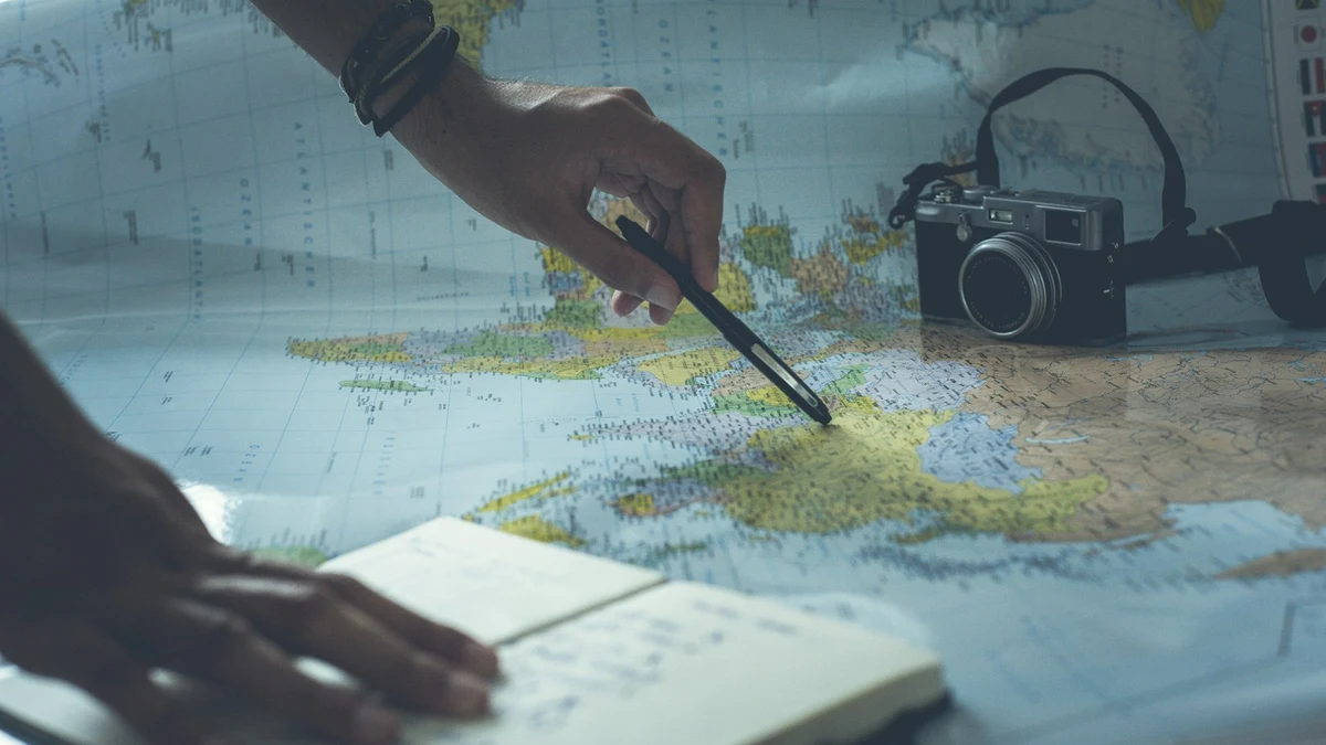 Two hands planning a route over an open paper map, with a notebook alongside