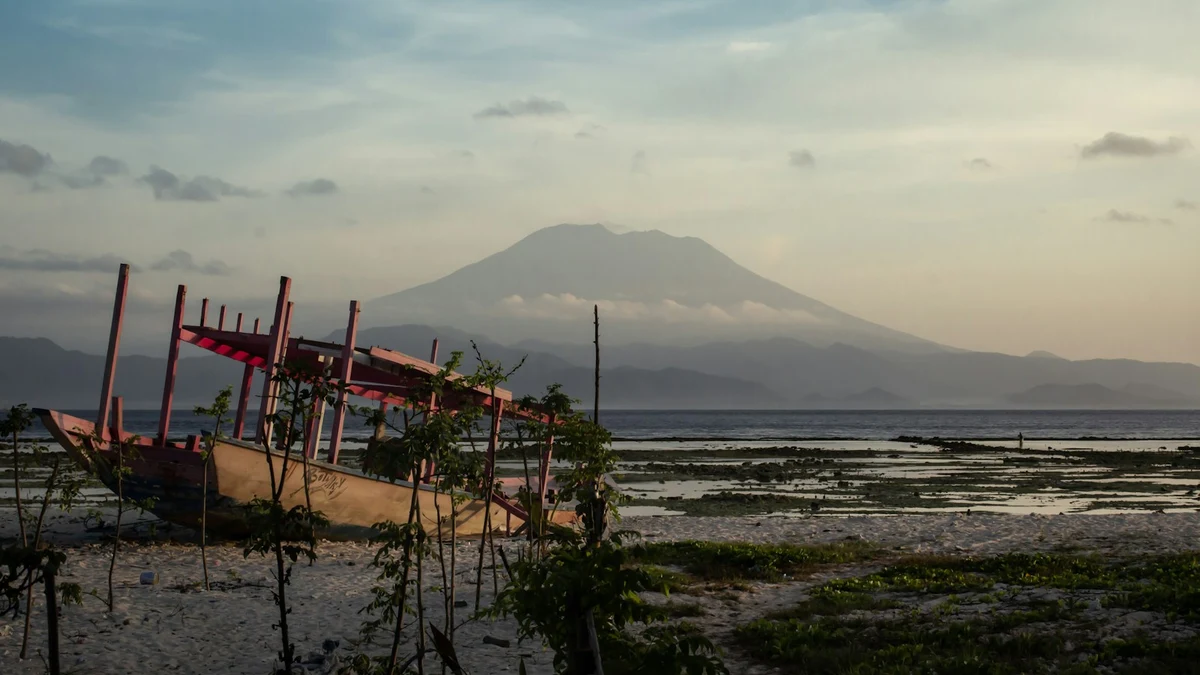 A beached outrigger boat at low tide with a volcano across the strait at dusk