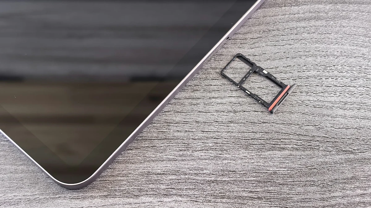 An empty SIM card tray lying on a wooden table next to the corner of a smartphone