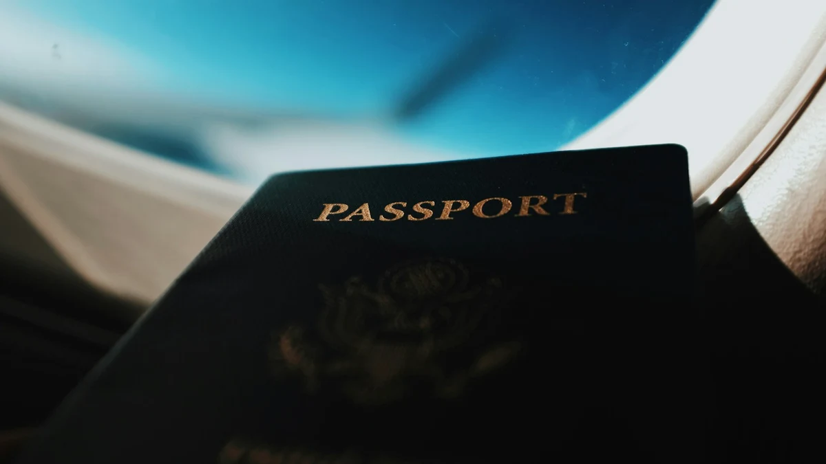 A dark passport with gold lettering held against the window of an aircraft cabin