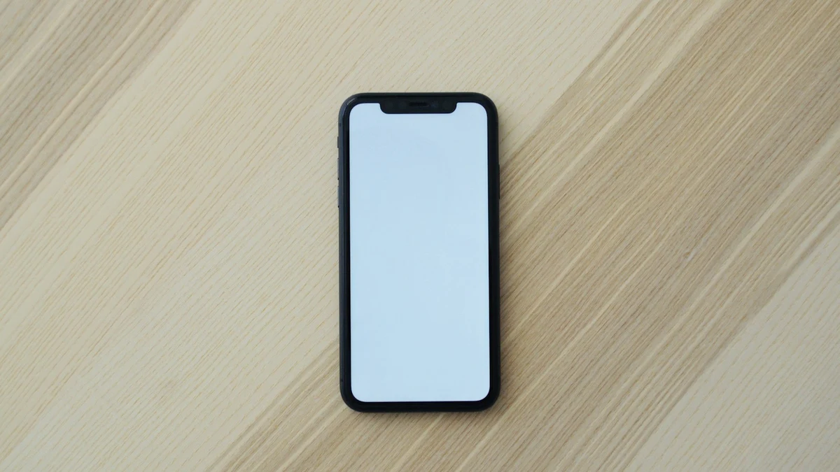 A smartphone with a blank white screen lying flat on a light wooden table