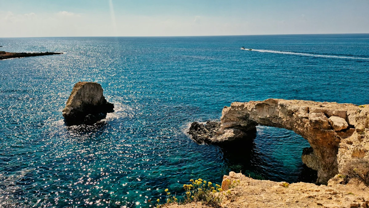 Natural rock arch at Cape Greco in Cyprus above clear blue water, with a boat in the distance