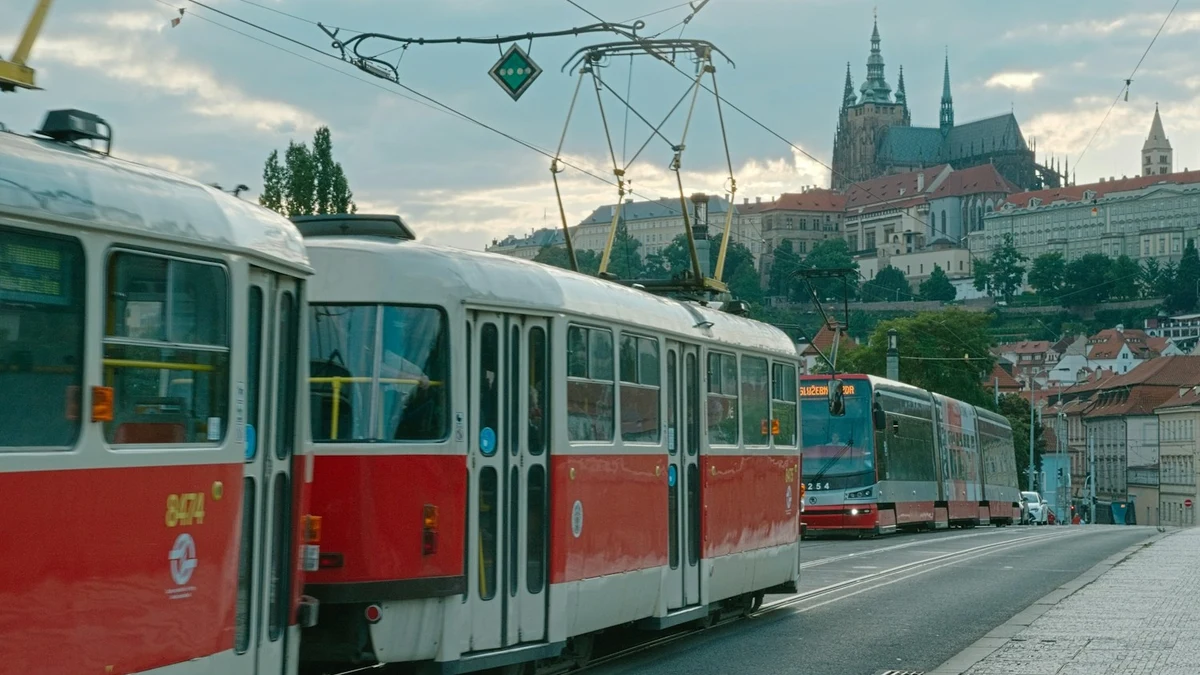 Red and white Prague trams on a street below the spires of St Vitus Cathedral and Prague Castle