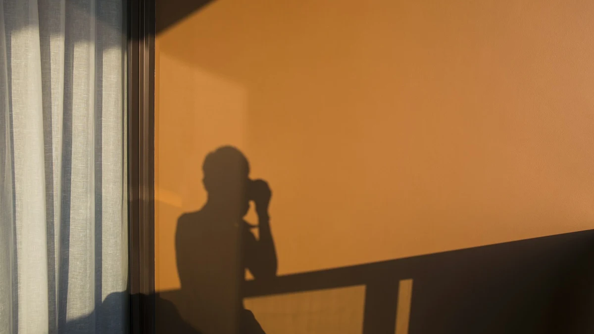 The shadow of a person holding a phone, cast across a sunlit orange wall