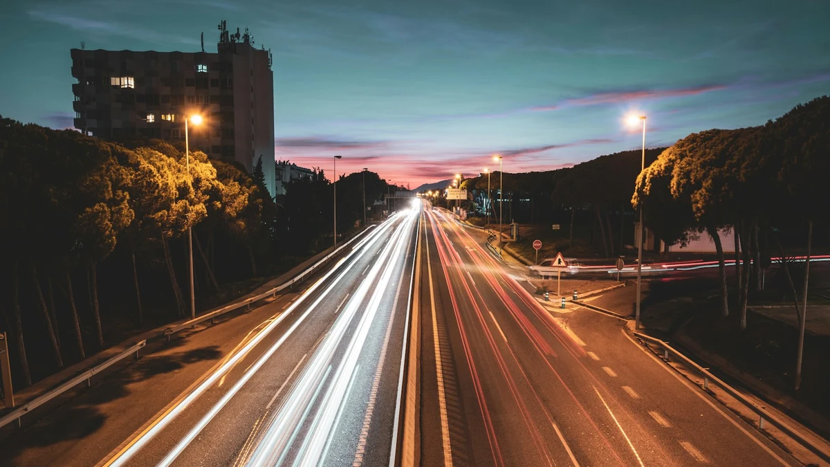 Light trails from evening traffic on a road into a Spanish town, hills and a pink sunset behind
