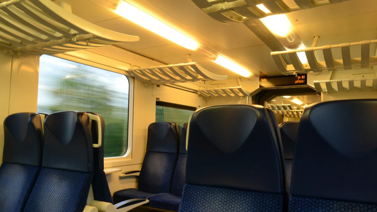 An empty second-class train carriage with blue seats and a blurred green landscape rushing past the window