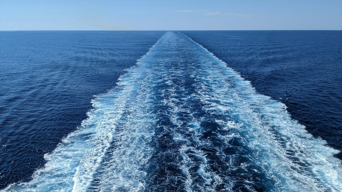 A ship's white wake stretching straight back to the horizon across a deep blue open sea