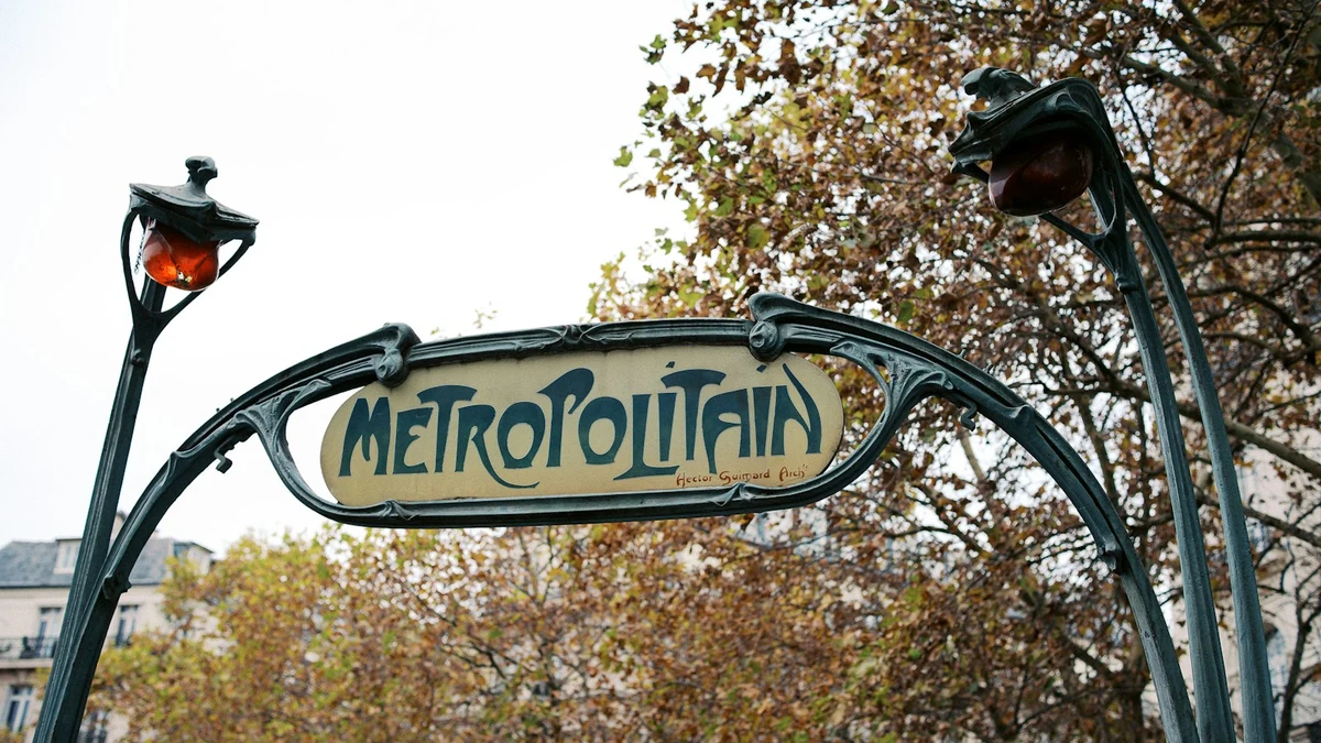 An art nouveau Metropolitain sign over a Paris metro entrance, autumn trees behind it