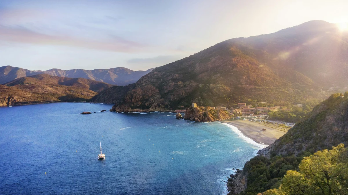 A Corsican bay at sunset with mountains behind a sheltered beach and a yacht at anchor