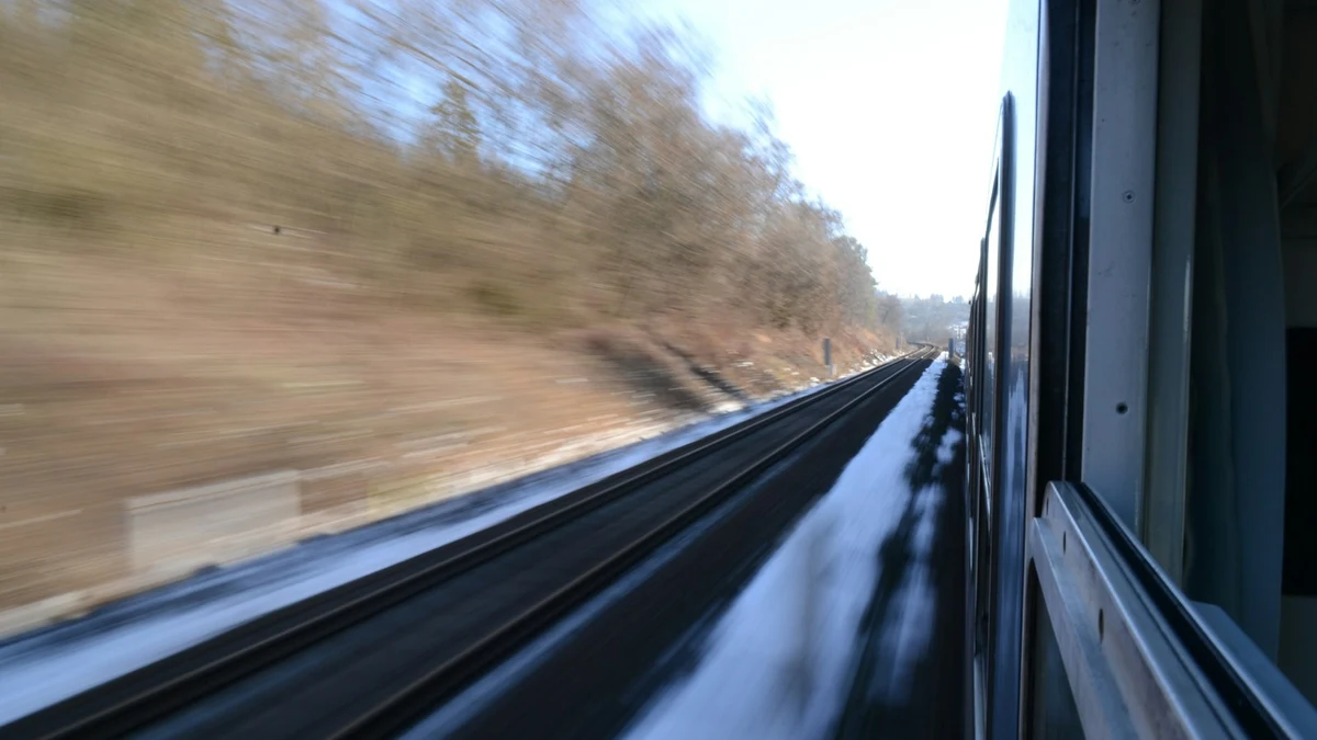 View from the window of a fast train: blurred trees, a parallel track and snow along the line
