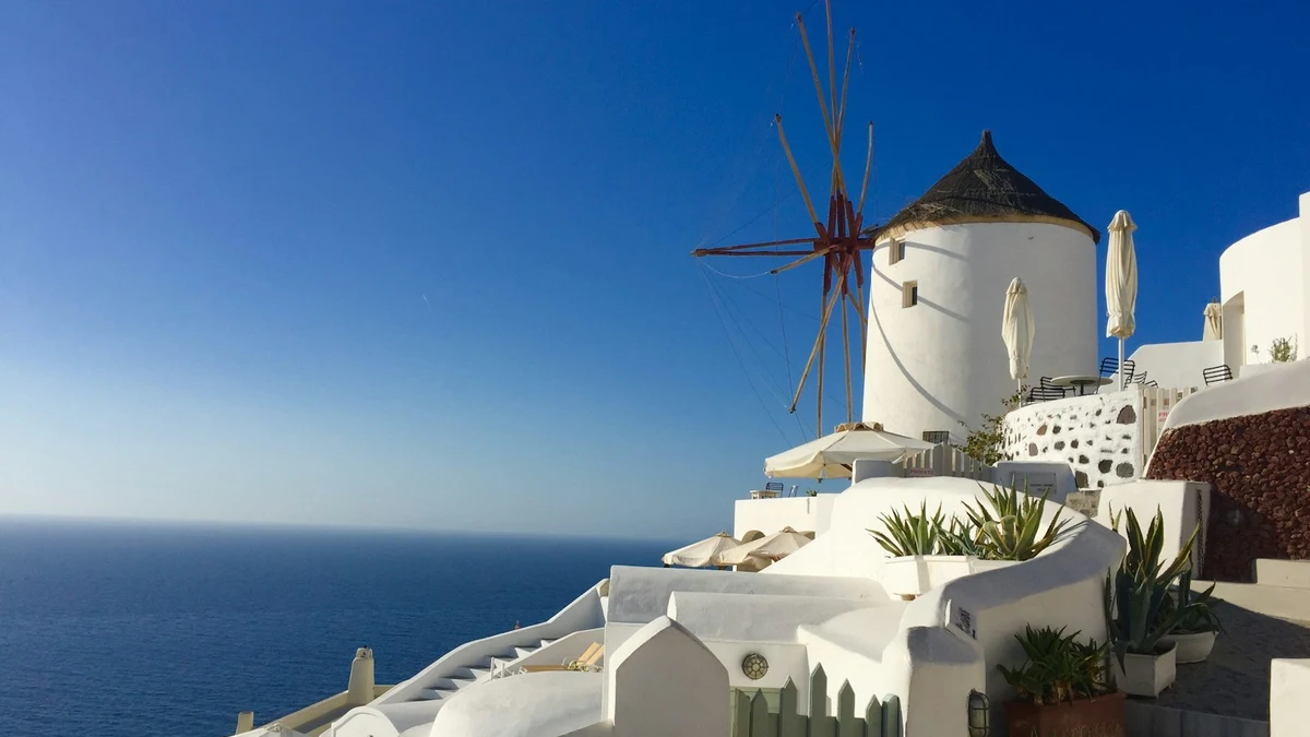 A whitewashed windmill above the open sea on a Cycladic island, terraces stepping down the slope