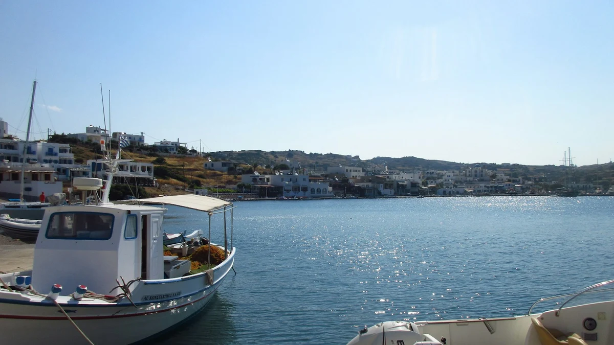 A small Greek fishing boat tied up at a stone quay, with an island town across the bay