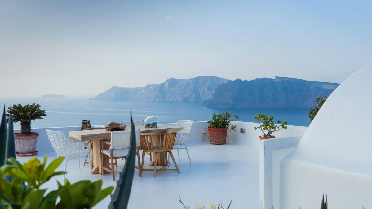 An empty whitewashed terrace with a dining table looking out across the sea to distant cliffs