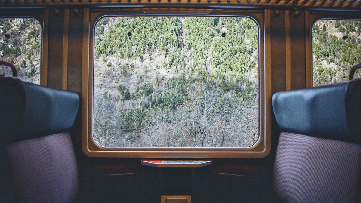 An empty compartment of an old train with blue seats and a large window framing a forested mountainside