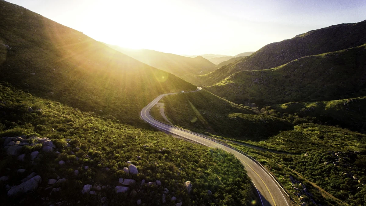 A road curving through green hills at sunrise, seen from the air