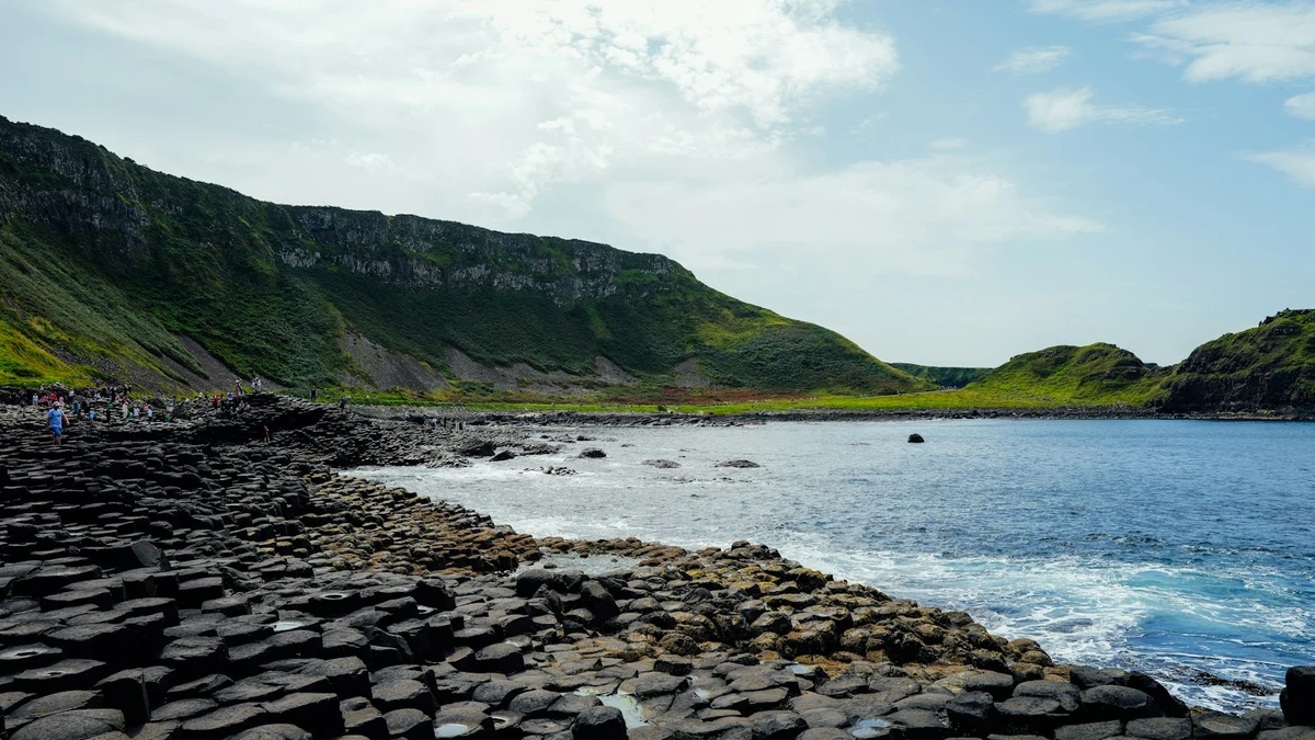 Hexagonal basalt columns of the Giant’s Causeway running into the sea below green cliffs in Northern Ireland