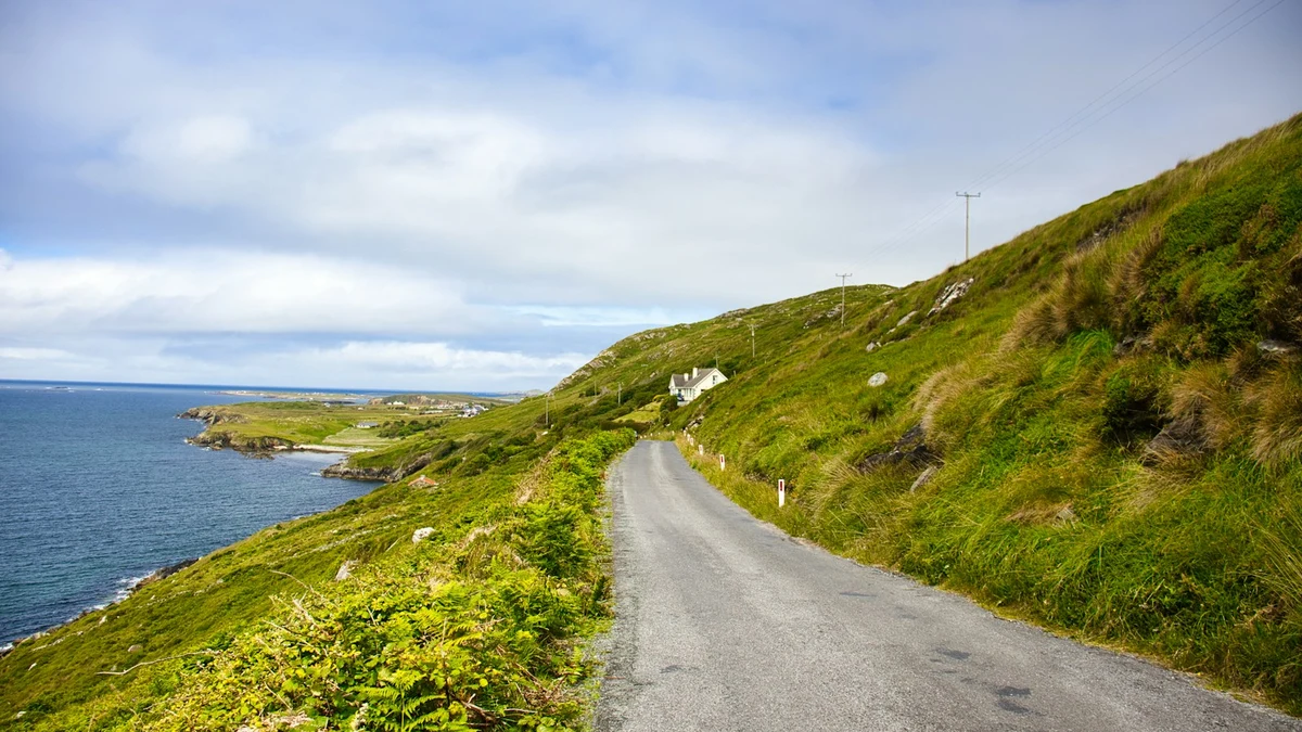 Narrow paved road climbing a green hillside above the Atlantic on Ireland’s west coast