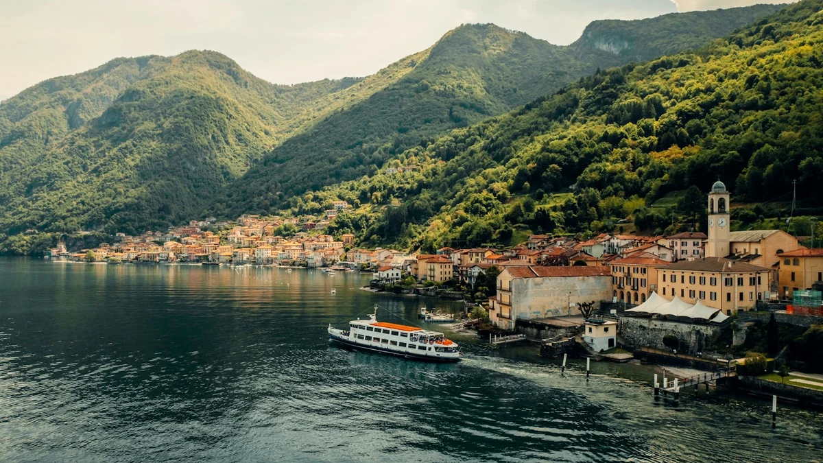 A passenger ferry crossing Lake Como past a lakeside village and wooded hills
