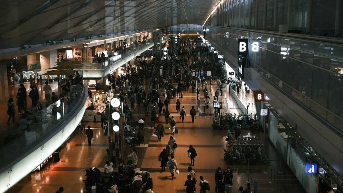 Travellers crossing a wide airport concourse in Tokyo seen from an upper level