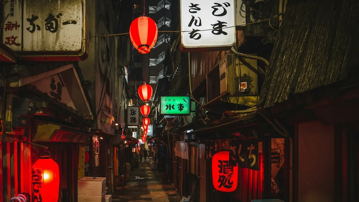 A narrow Japanese alley at night lined with small restaurants and glowing paper lanterns