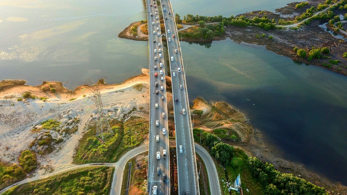 Aerial view of a busy multi-lane road bridge crossing a narrow strait between two green shorelines
