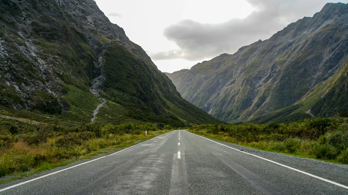 Empty two-lane road running through a green valley between steep mountains in Fiordland, New Zealand