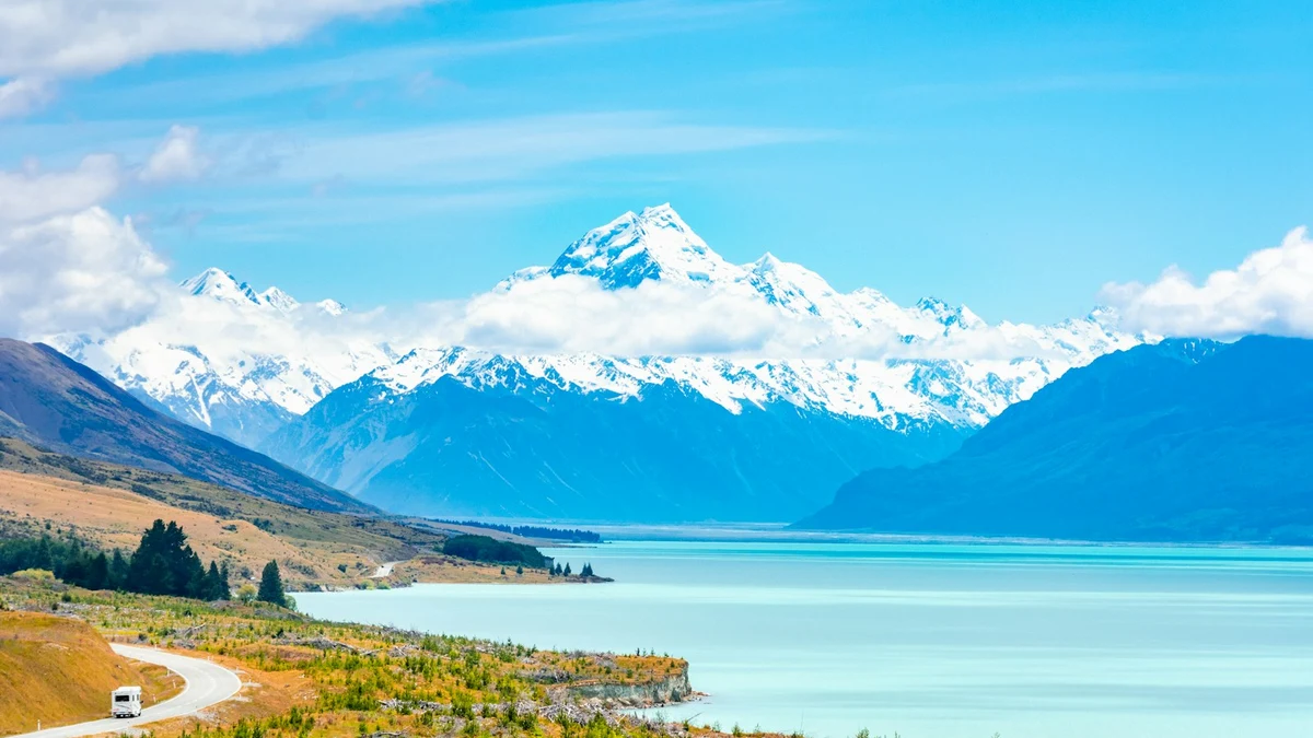 Campervan on a winding road above the turquoise water of Lake Pukaki, with snow-covered Aoraki Mount Cook behind