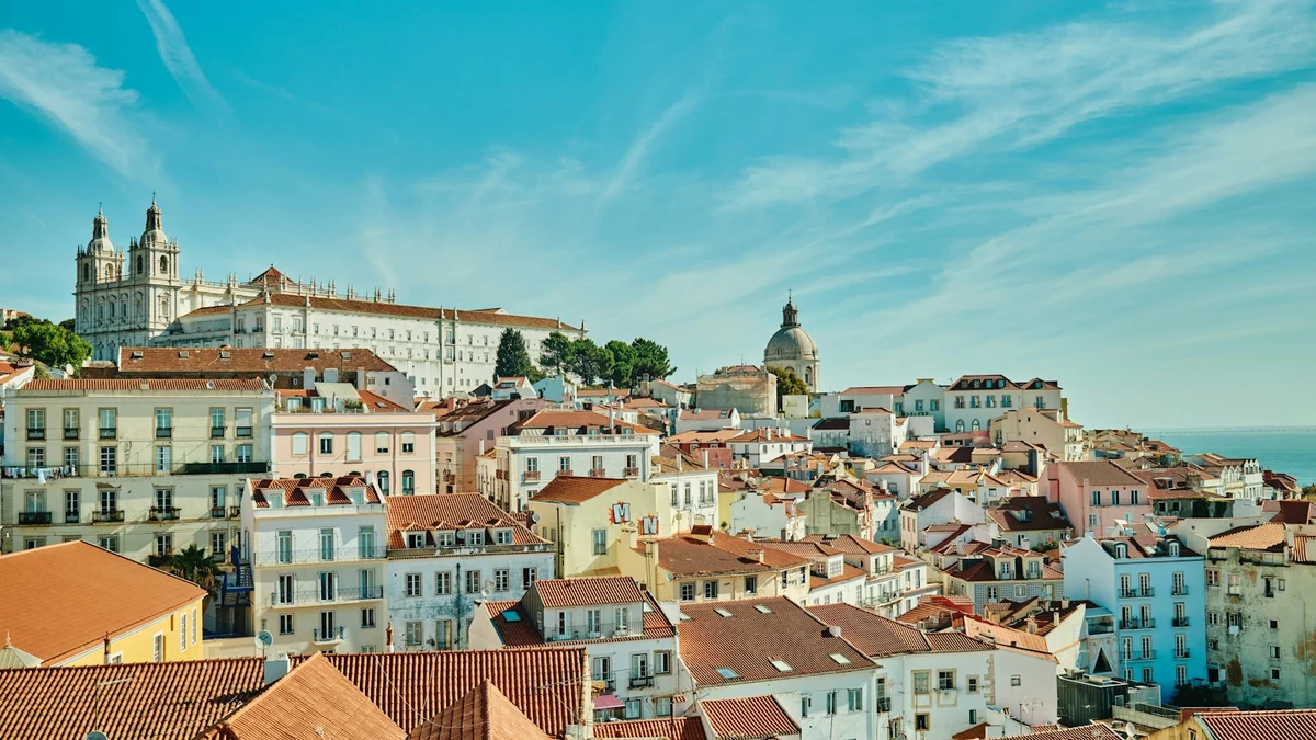 Pastel houses and terracotta roofs of Lisbon stepping down towards the river under a bright sky