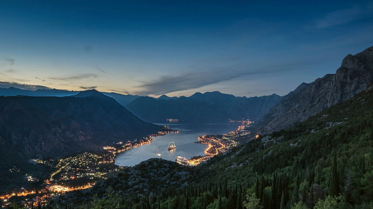 The Bay of Kotor at dusk, town lights tracing the shoreline beneath dark mountains
