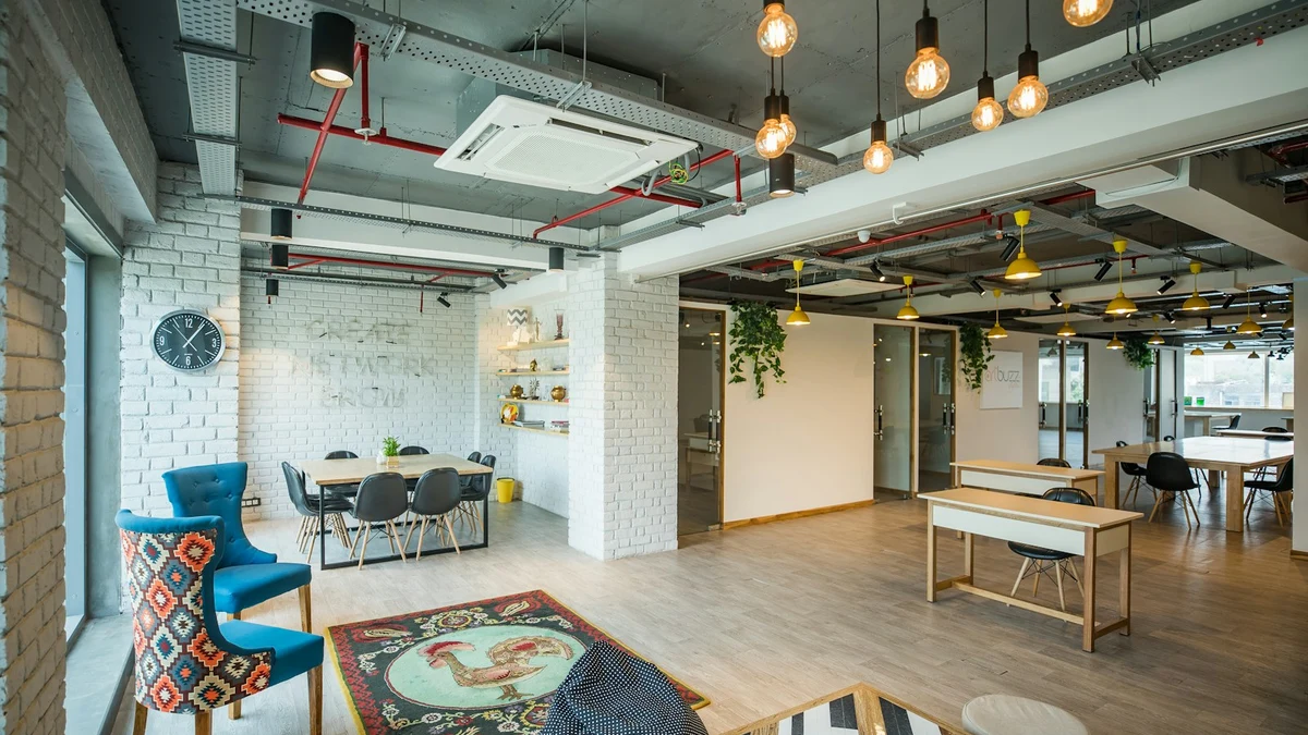 An empty coworking space with long tables, pendant lights and exposed ceiling pipes