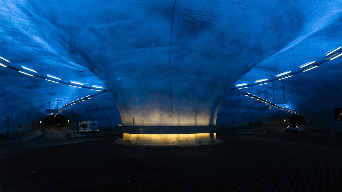 Underground roundabout in a Norwegian road tunnel, its rock ceiling lit in blue with a warm light at the base of the central pillar