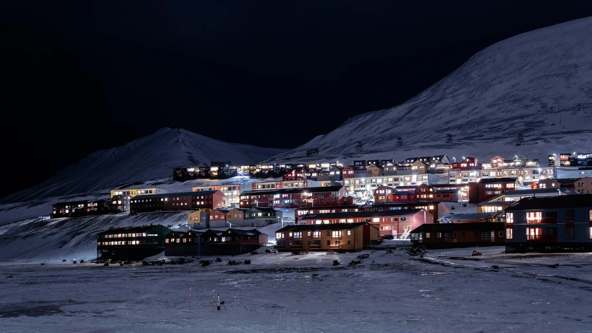 Lights of Longyearbyen houses under a snow-covered mountainside during the dark polar night in Svalbard