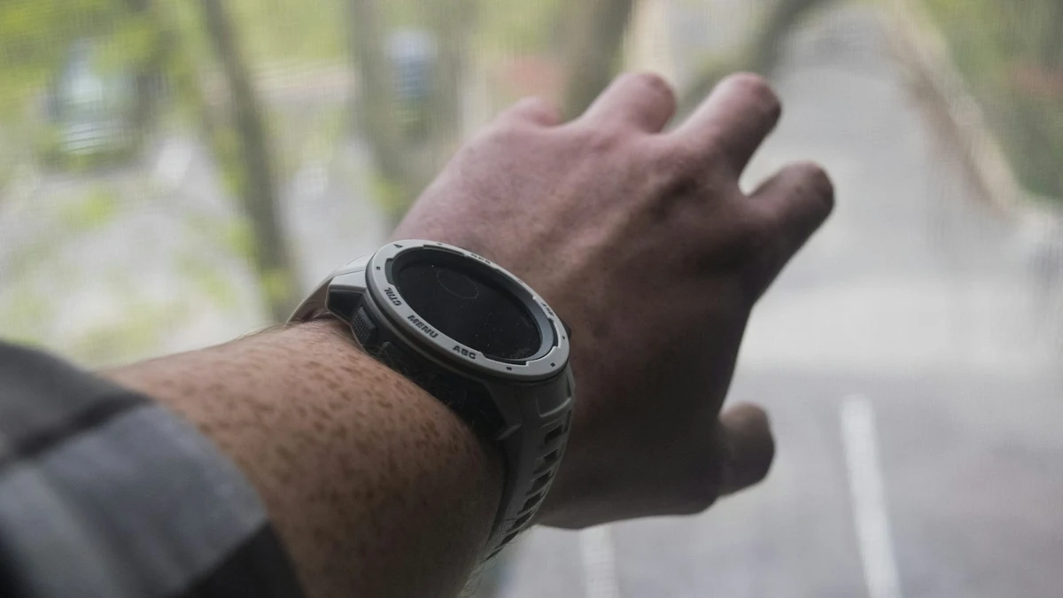 Wrist with a sports smartwatch, screen off, blurred trees behind