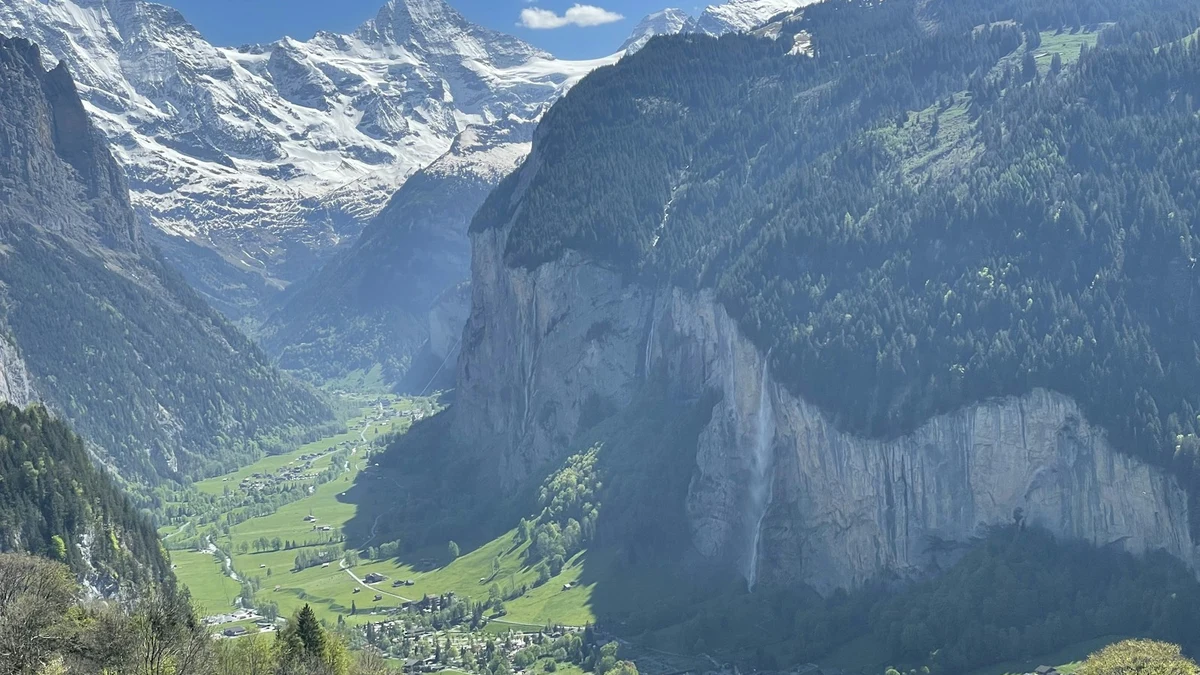A deep alpine valley with sheer cliffs, a waterfall and a village on the green valley floor