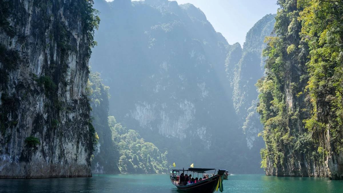 A longtail boat crossing green water between steep limestone cliffs