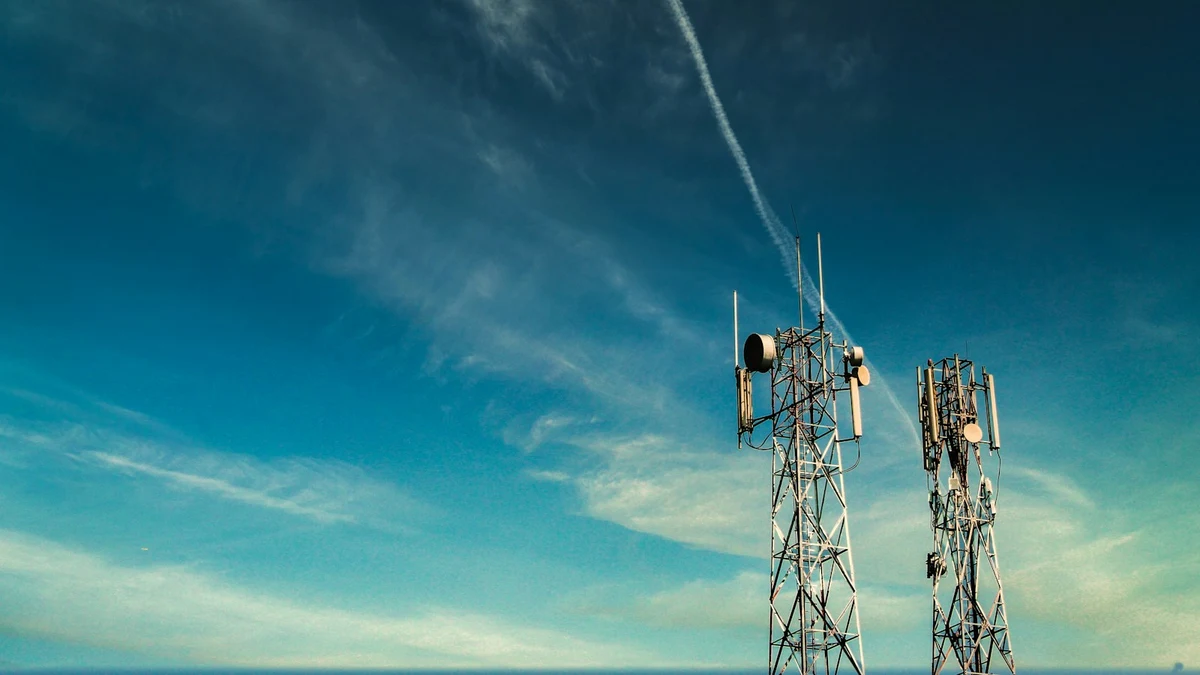 Two lattice cell towers with antennas against a blue sky with a vapour trail