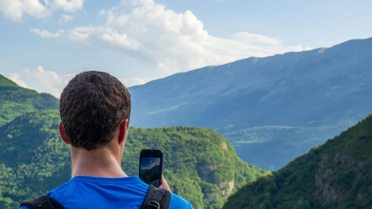 A traveller seen from behind photographing green mountains with a smartphone