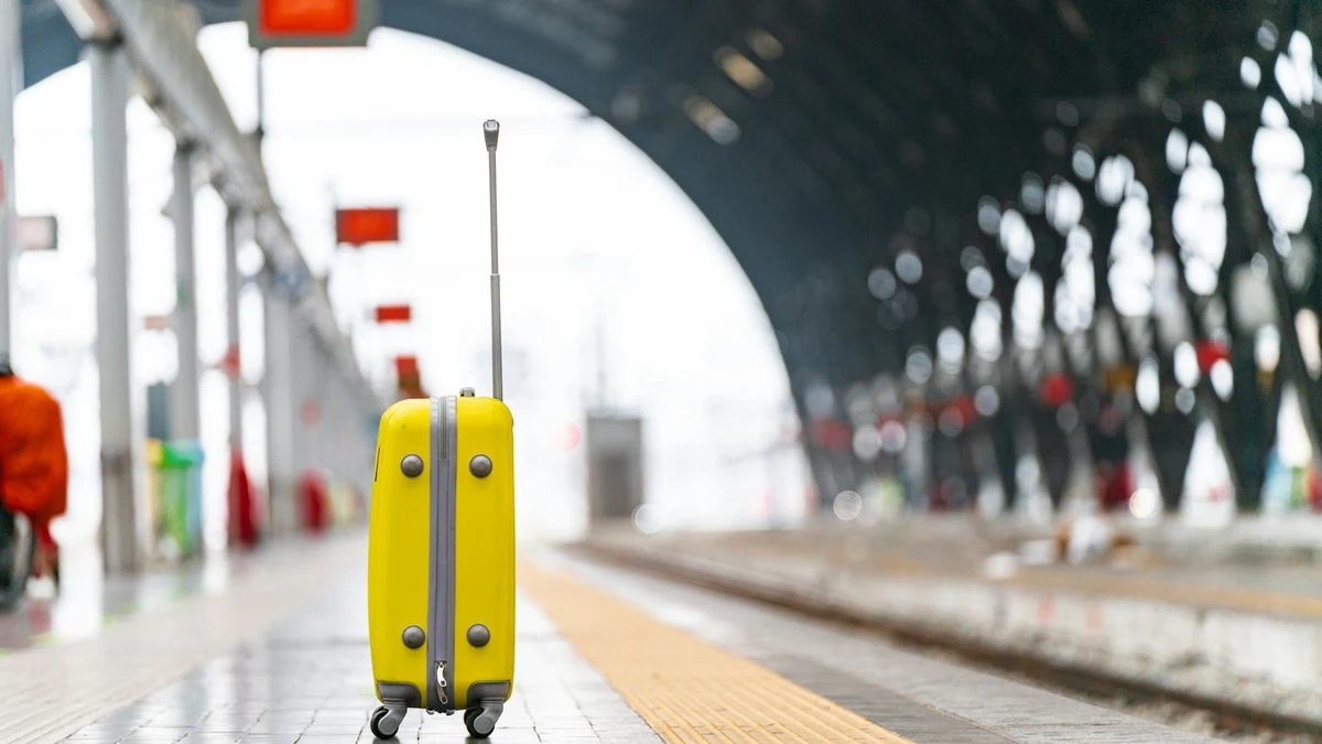A single yellow suitcase standing on an empty European railway station platform