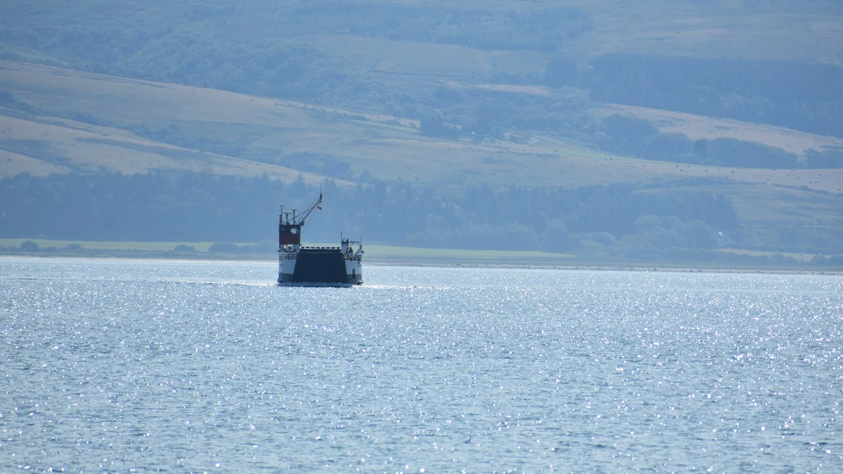 A small ferry crossing open water in front of low green hills