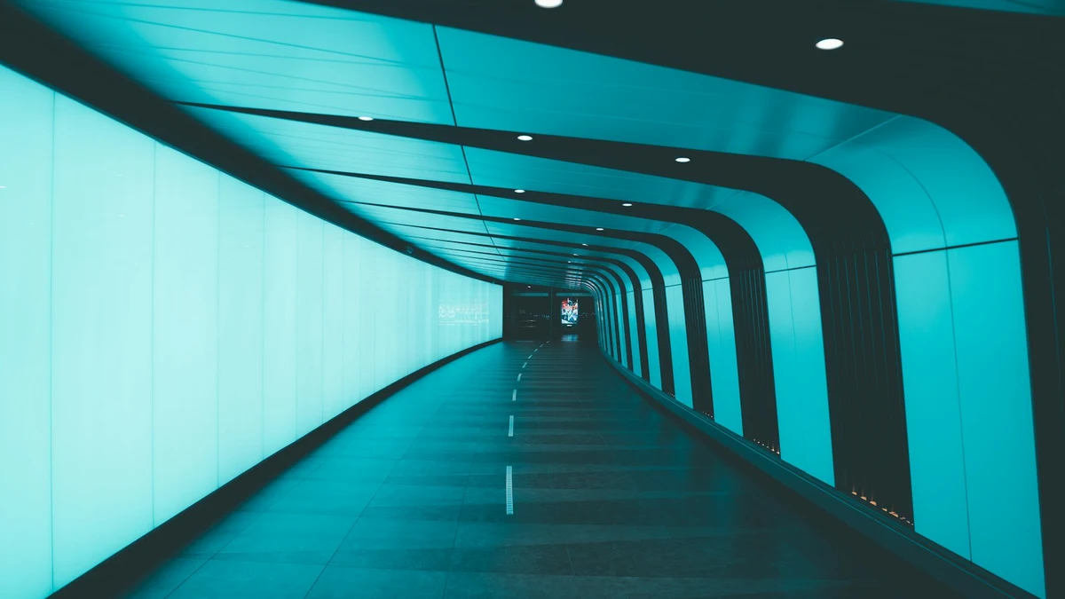 A curved pedestrian underpass lit by a glowing turquoise wall, empty of people