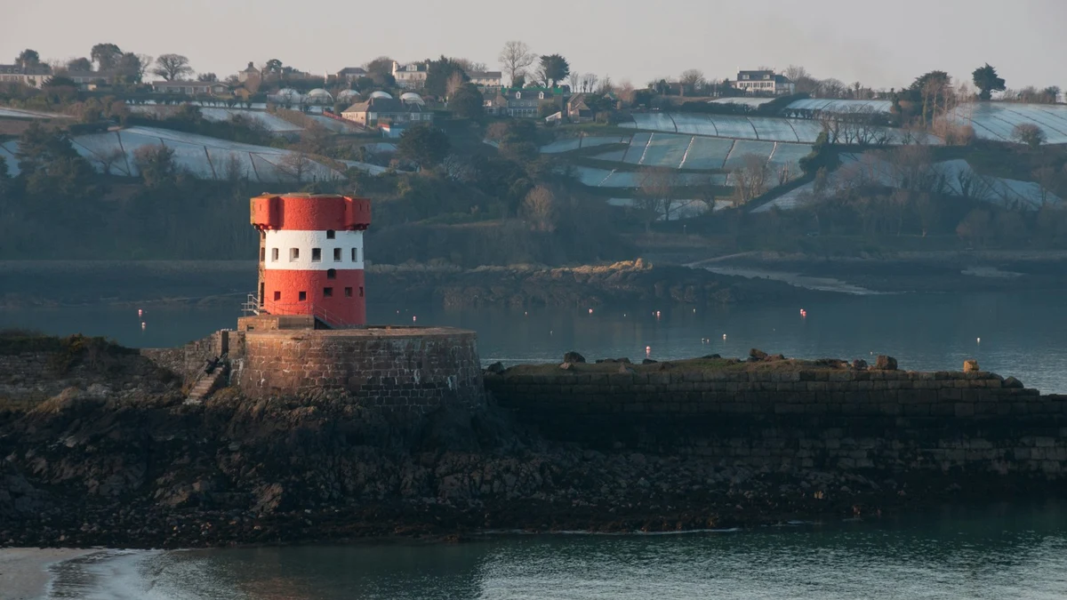 A red and white Jersey watchtower on a rocky headland above a calm bay at dawn